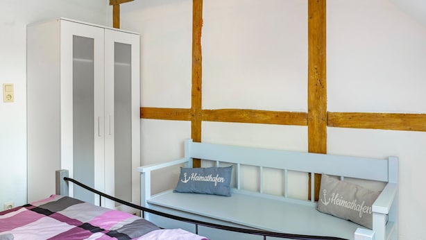 Un dormitorio con cama, armario y un banco con almohadones.