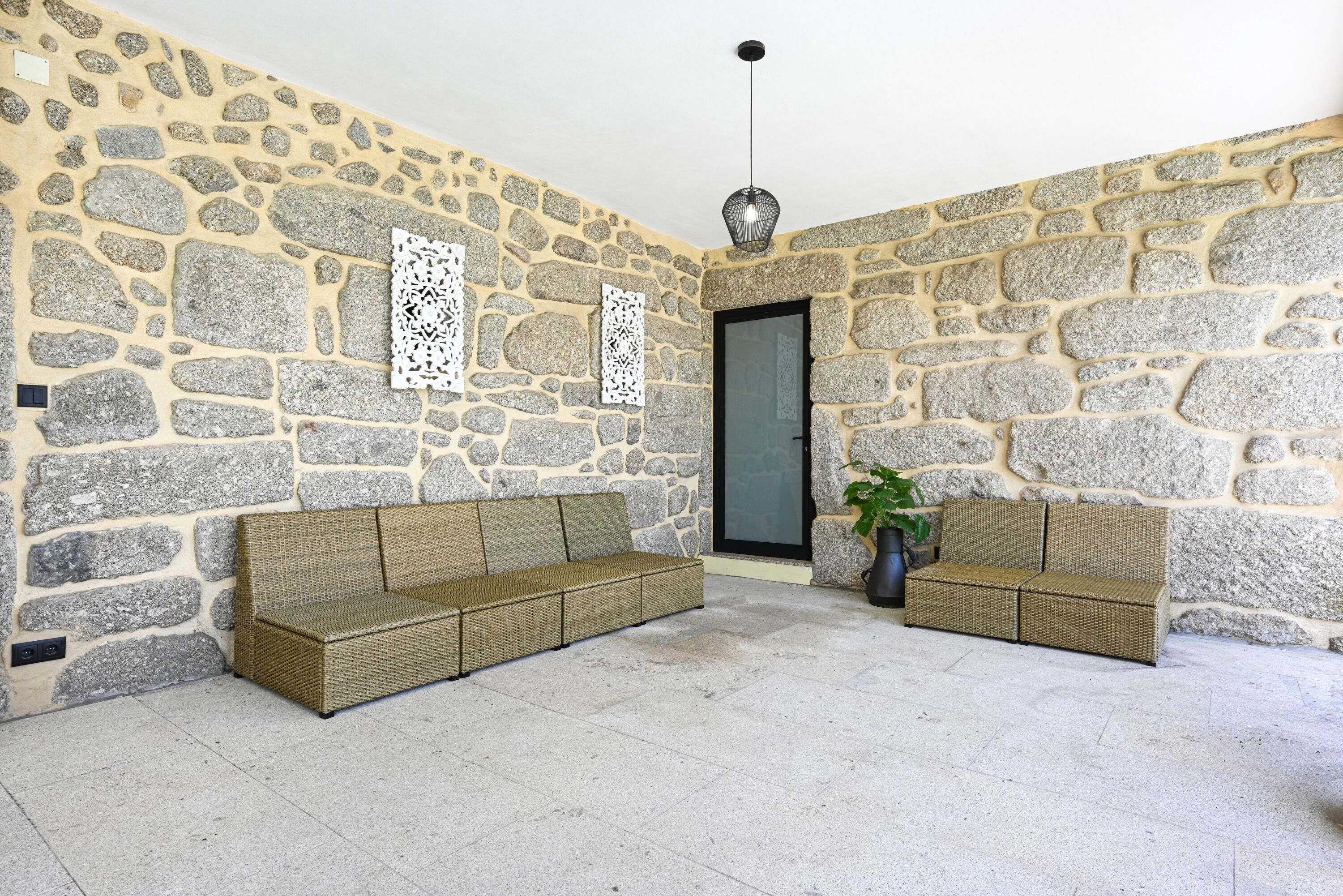 Ein Zimmer mit Steinwänden, zwei Korbschaukeln, einem Blumentopf und einer Pendelleuchte.