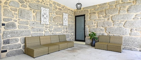 Una habitación con paredes de piedra, dos sofás de mimbre, una planta en maceta y una lámpara colgante.