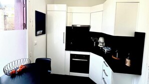A compact kitchen with white cabinets, a black countertop, and a window with blinds. - 90-square-meter apartment in the city center, 10 minutes from the train station, 200 meters from the cathedral (Quimper)