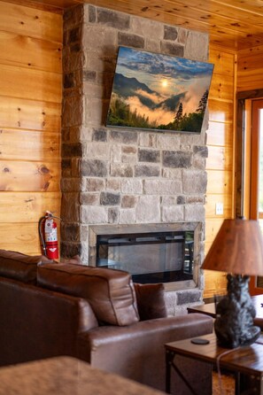 A stone fireplace with a painting above it, a leather sofa, a fire extinguisher, and a lamp. - Grand Splash Cabin | Hot Tub, Pool, View, GAMES! (Sevierville)