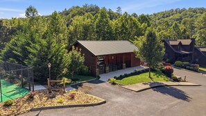 A log cabin with a metal roof, surrounded by a well-maintained lawn and a fence. - Grand Splash Cabin | Hot Tub, Pool, View, GAMES! (Sevierville)