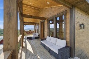 A wooden deck with a sofa and a chair, large windows, and a view of the landscape. - Grand Splash Cabin | Hot Tub, Pool, View, GAMES! (Sevierville)