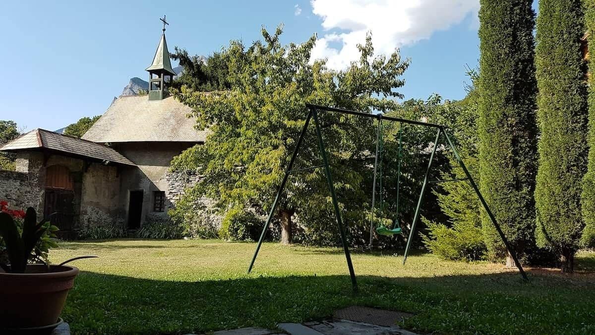 A stone building with a conical roof, a swing set, and a well-maintained garden.