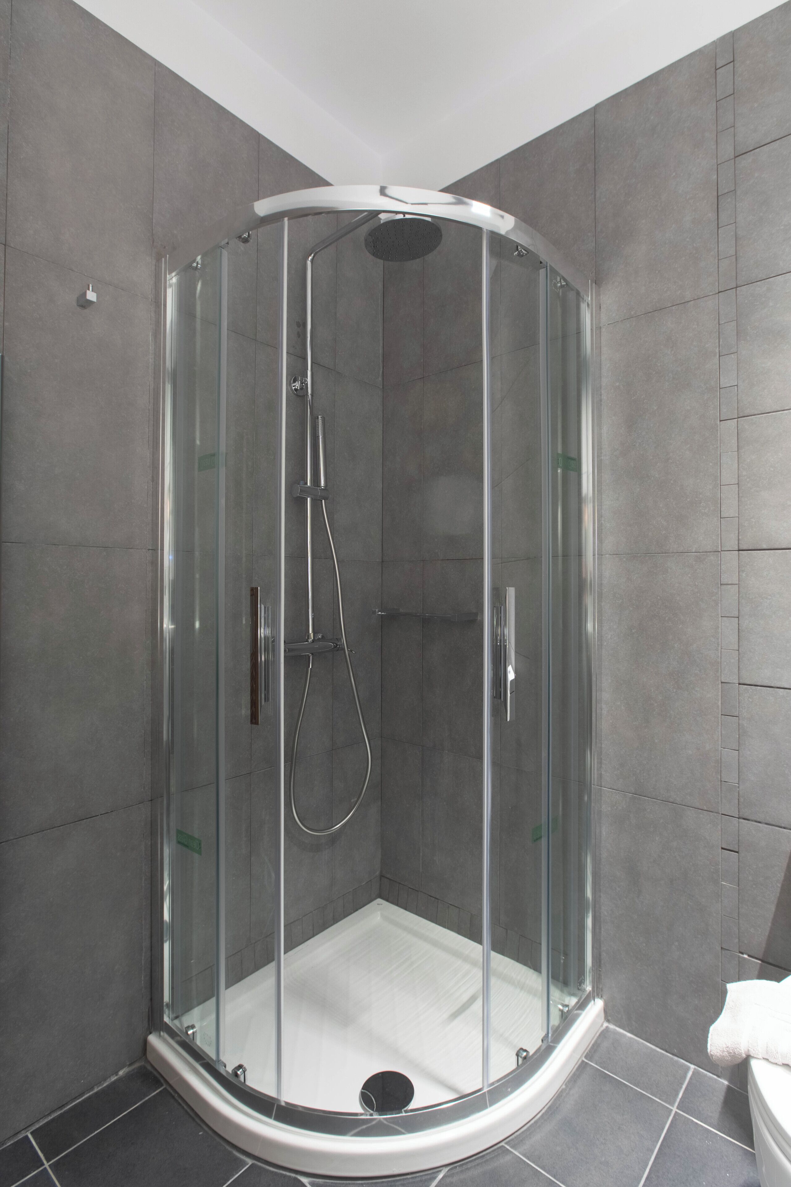 A glass-enclosed shower stall with a curved design, a handheld showerhead, and a wall-mounted faucet.
