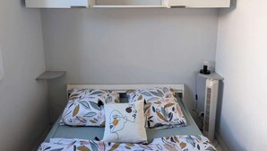 Ett litet, välordnat sovrum med en enkelsäng, ett sängbord, en hylla på väggen och en vägglampa.