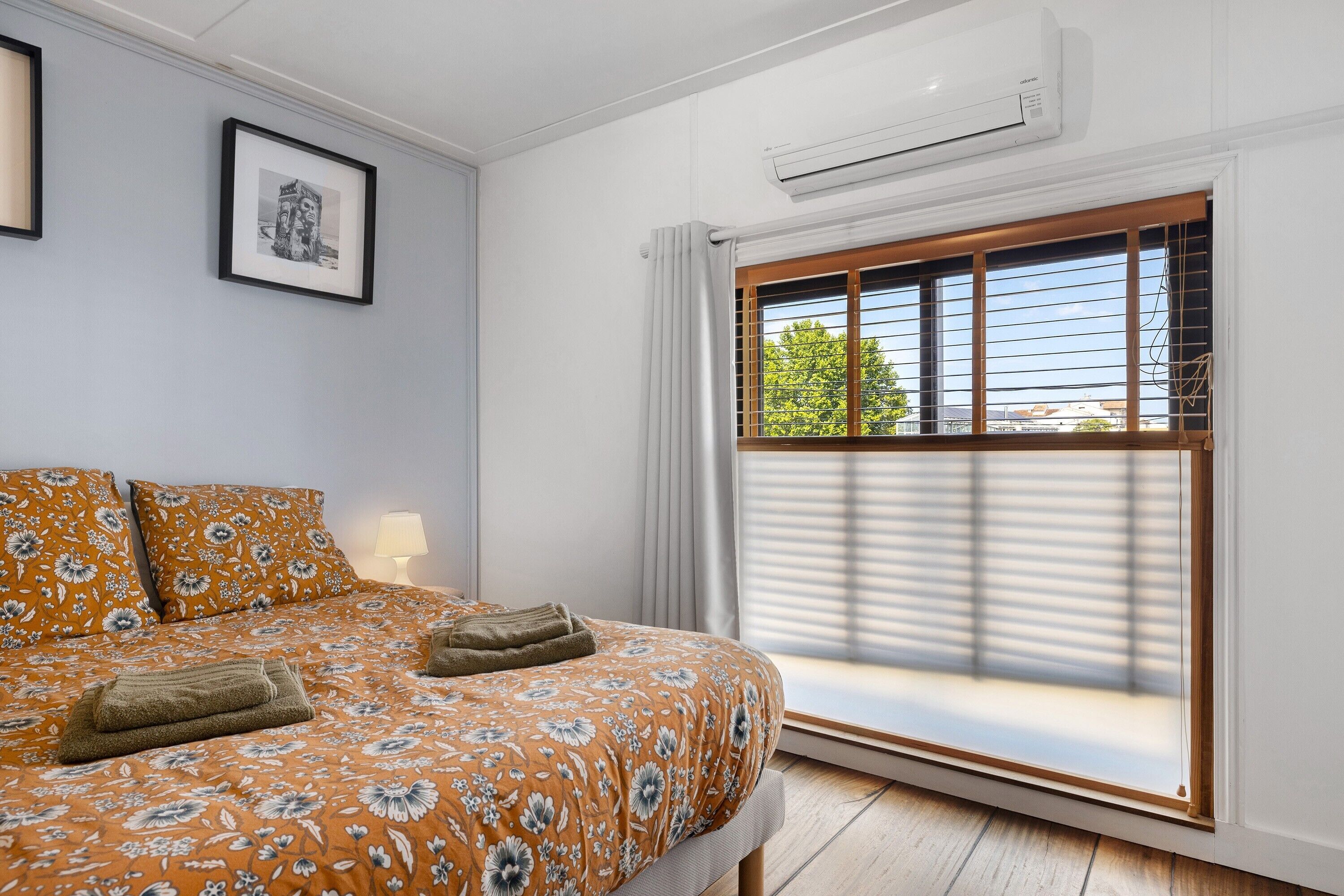 Ein Schlafzimmer mit einem Bett, einem Fenster mit Jalousien, einer Klimaanlage und einem gerahmten Bild an der Wand.