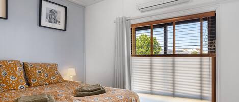 Ein Schlafzimmer mit einem Bett, einem Fenster mit Jalousien, einer Klimaanlage und einem gerahmten Bild an der Wand.