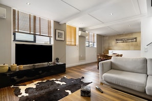 A living room with a flat-screen TV, a sofa, a cowhide rug, and wooden flooring. - Holiday Home 'Esprit Chic-Calme-Climatisation' with Private Garden, Wi-Fi and Air Conditioning (Pessac)