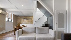 A modern living room with a sofa, a dining table, and a staircase. - Holiday Home 'Esprit Chic-Calme-Climatisation' with Private Garden, Wi-Fi and Air Conditioning (Pessac)