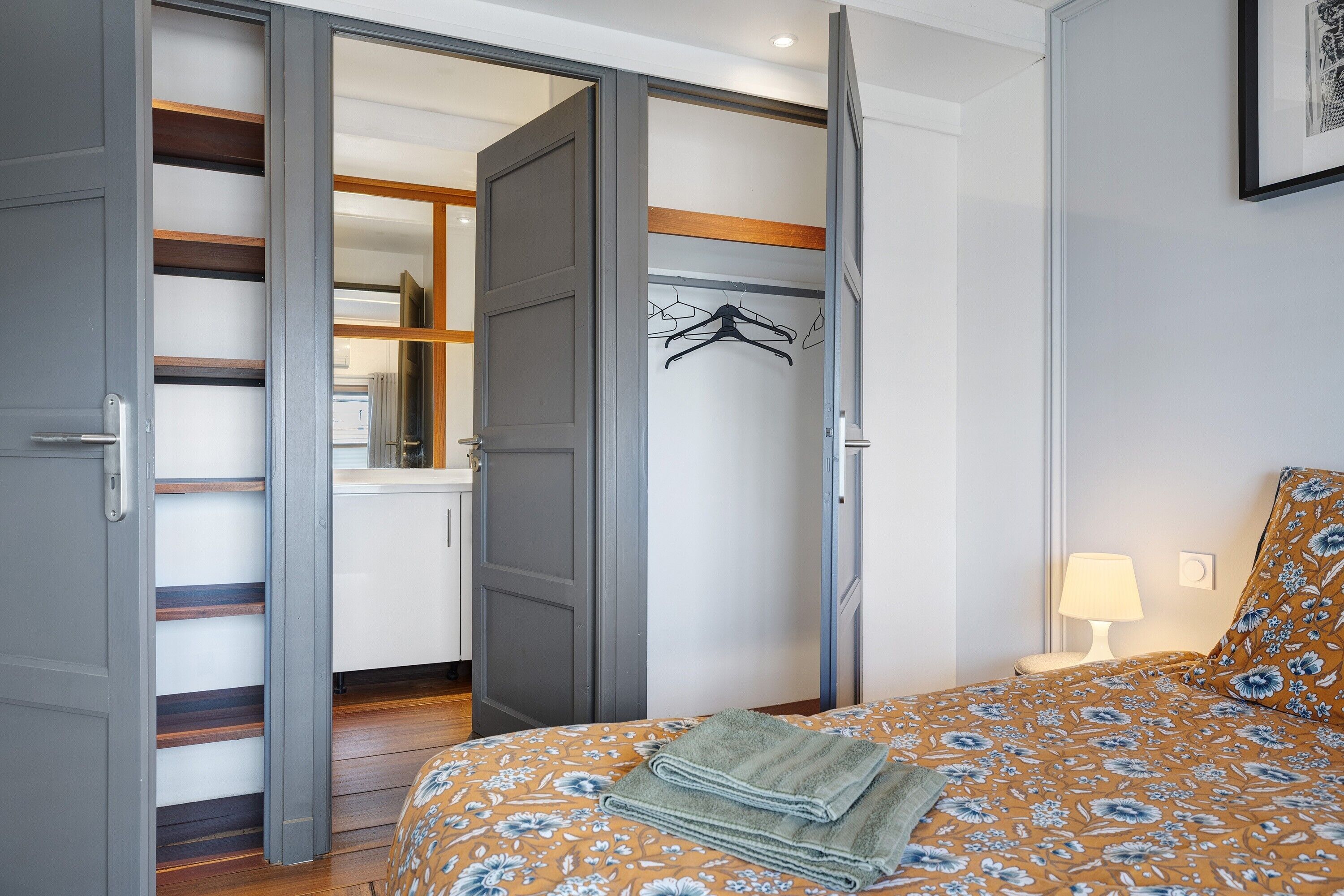 A bedroom with a bed, a bedside table, a lamp, and a wardrobe with a mirror.