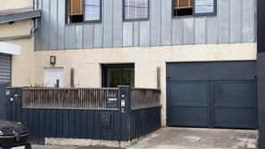 A two-story building with a garage door, a wooden fence, and a mailbox. - Holiday Home 'Esprit Chic-Calme-Climatisation' with Private Garden, Wi-Fi and Air Conditioning (Pessac)