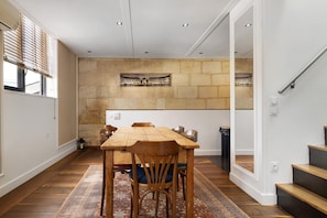 A dining area with a wooden table and chairs, a stone wall with a picture, and a staircase. - Holiday Home 'Esprit Chic-Calme-Climatisation' with Private Garden, Wi-Fi and Air Conditioning (Pessac)