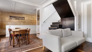 A modern living room with a sofa, a dining table with chairs, a staircase, and a wall with a picture. - Holiday Home 'Esprit Chic-Calme-Climatisation' with Private Garden, Wi-Fi and Air Conditioning (Pessac)