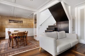 A modern living room with a sofa, a dining table with chairs, a staircase, and a wall with a picture. - Holiday Home 'Esprit Chic-Calme-Climatisation' with Private Garden, Wi-Fi and Air Conditioning (Pessac)