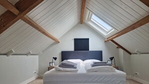 Una camera da letto con soffitto spiovente, un letto con cuscini e asciugamani, lampade sui comodini e una finestra.