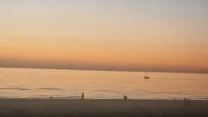 Una spiaggia con acque calme, una barca in lontananza e persone che passeggiano sulla riva.