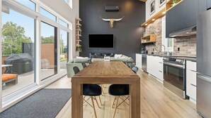 Ett modernt kök med ett stort matbord, inbyggda vitvaror och en tv som är monterad på väggen.