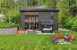 Ein modernes, zweistöckiges Haus mit großem Glasflurtür, einer Terrasse mit Sitzgelegenheiten und einem Whirlpool.