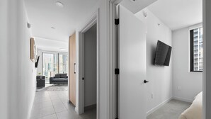Un interior moderno con un pasillo que conduce a una sala de estar, un televisor de pantalla plana en la pared y un ventanal grande.