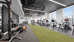 Un gimnasio con equipo de levantamiento de pesas, máquinas de cardio y una zona alfombrada en color verde.