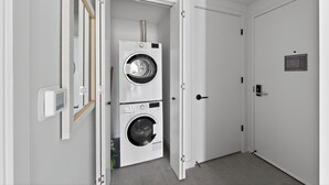 Un lavadero con dos lavadoras apiladas, una puerta con cerradura y un interruptor de luz en la pared.