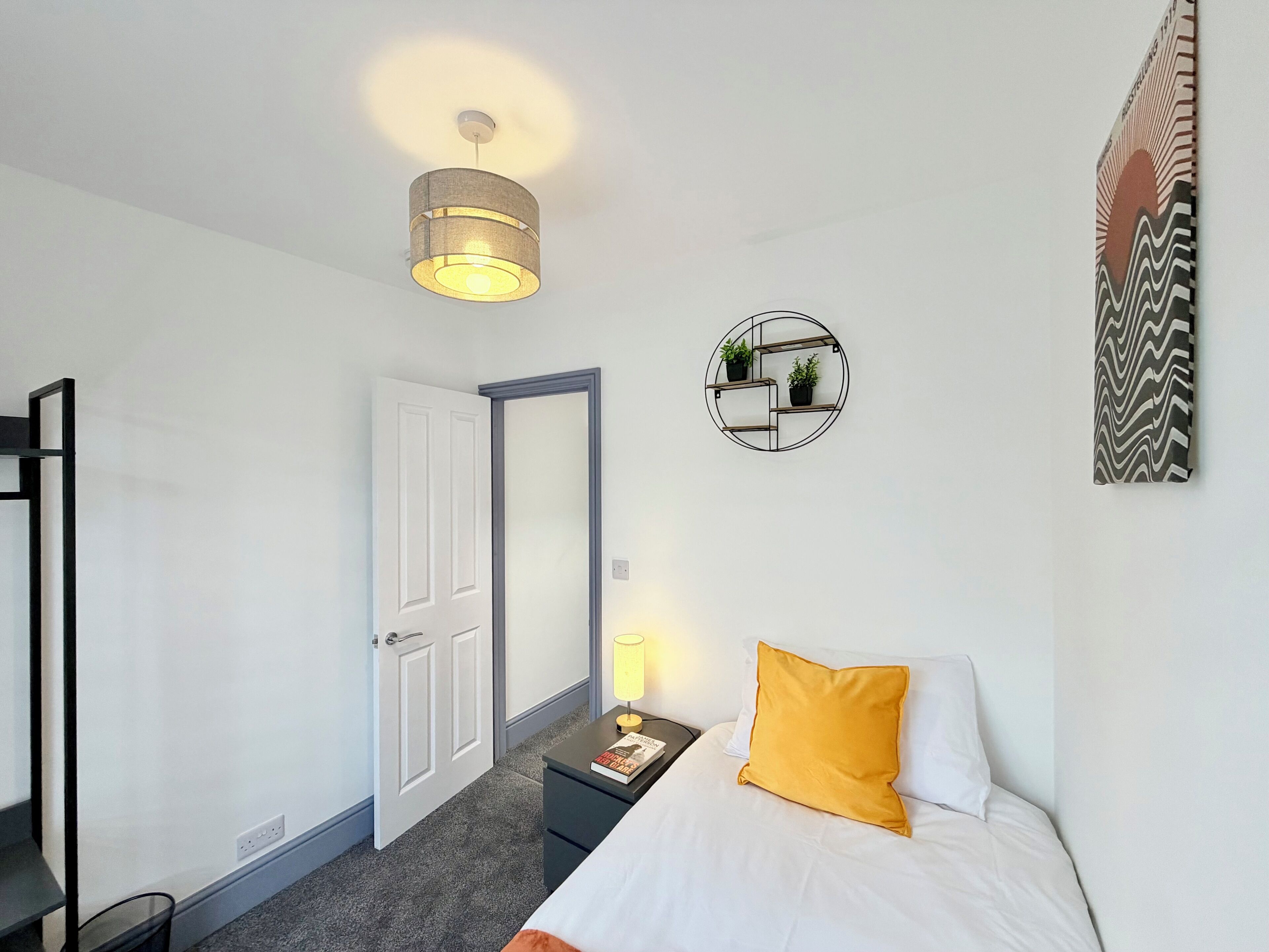 Une chambre d’hôtel avec un lit, une table de chevet, une lampe, des œuvres d’art mural et une porte.