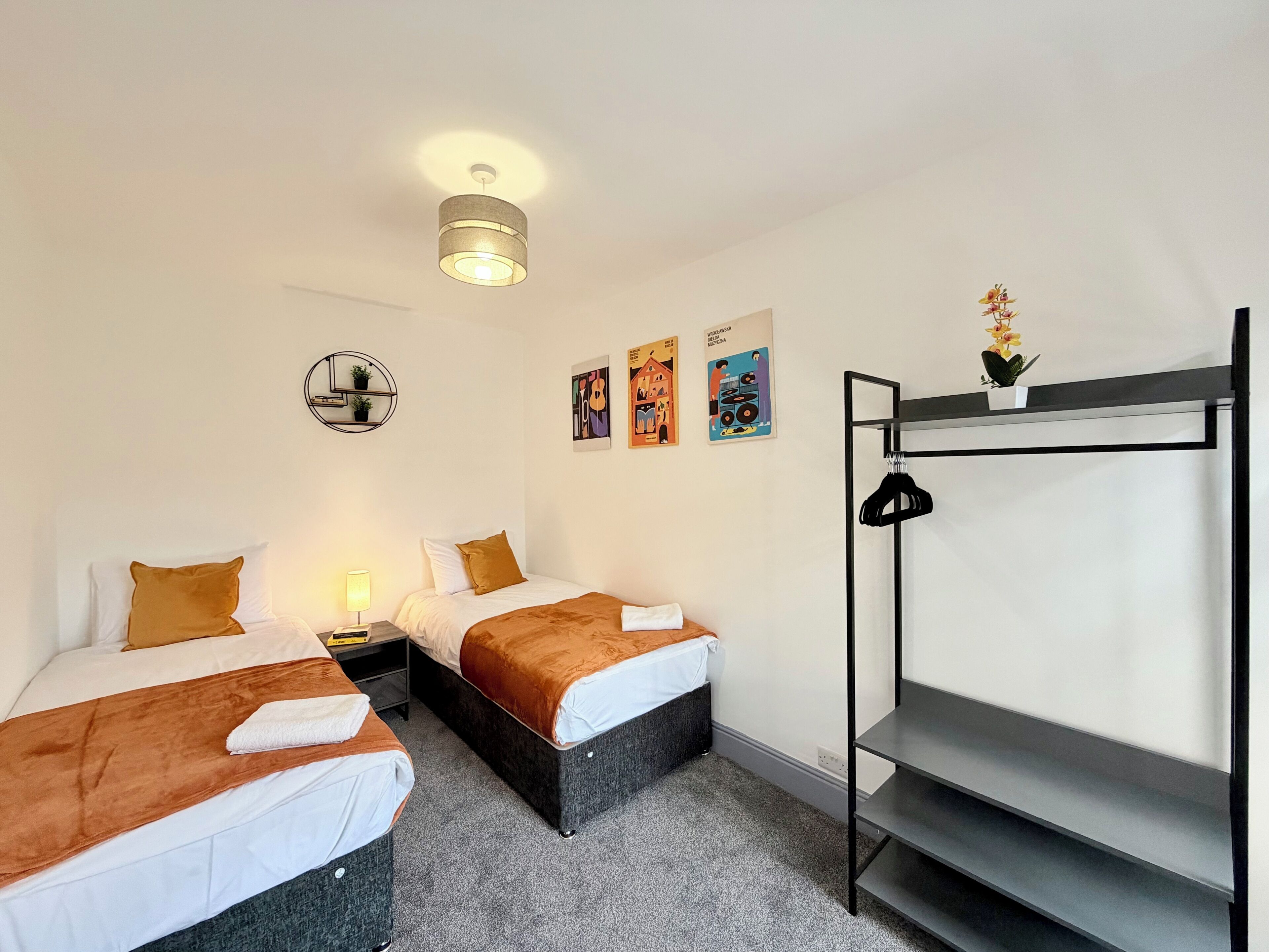 Une chambre d’hôtel avec deux lits, un petit bureau, une étagère fixée au mur et un luminaire au plafond.