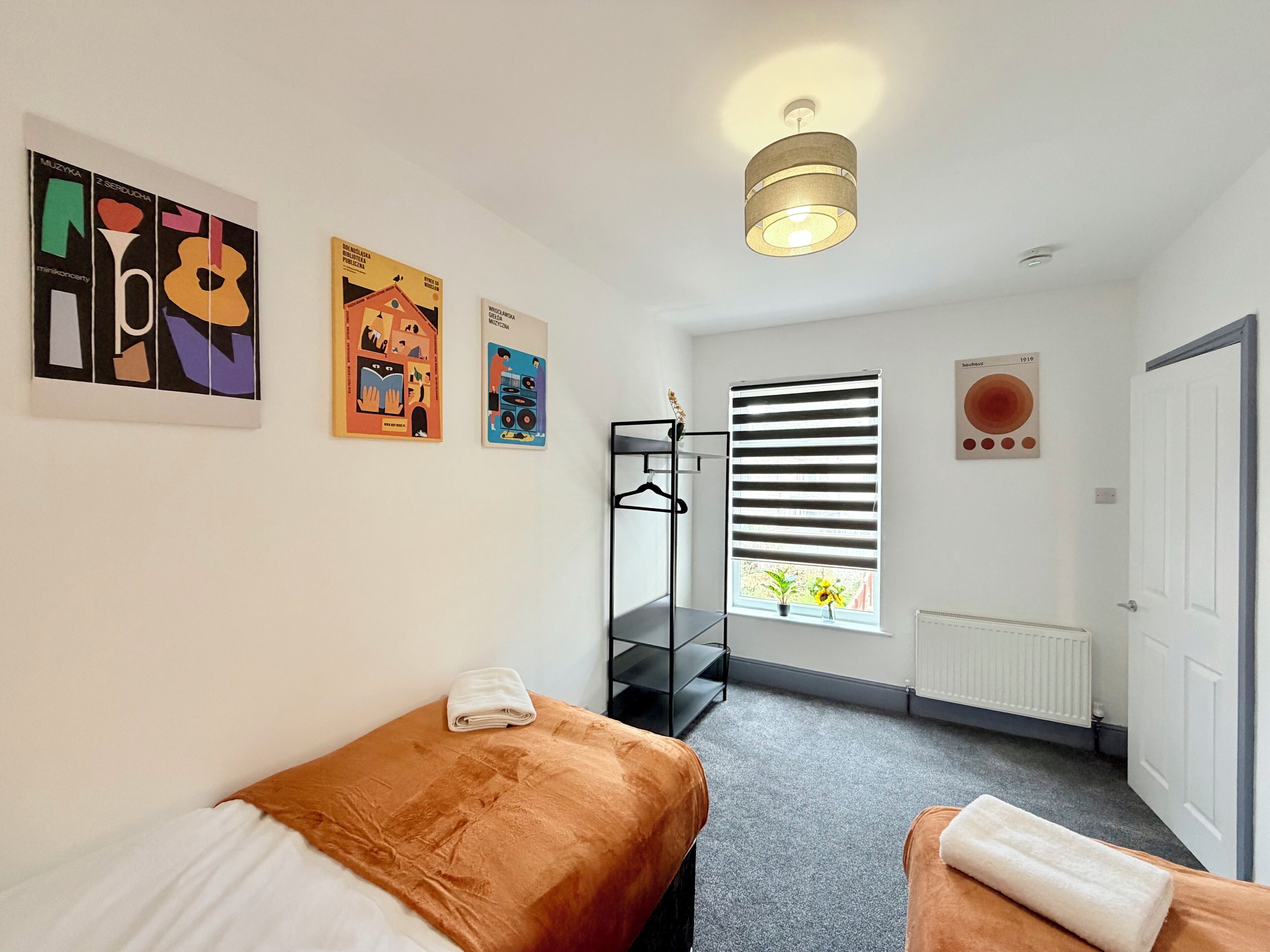 A room with a bed, a window with blinds, a radiator, and wall art.
