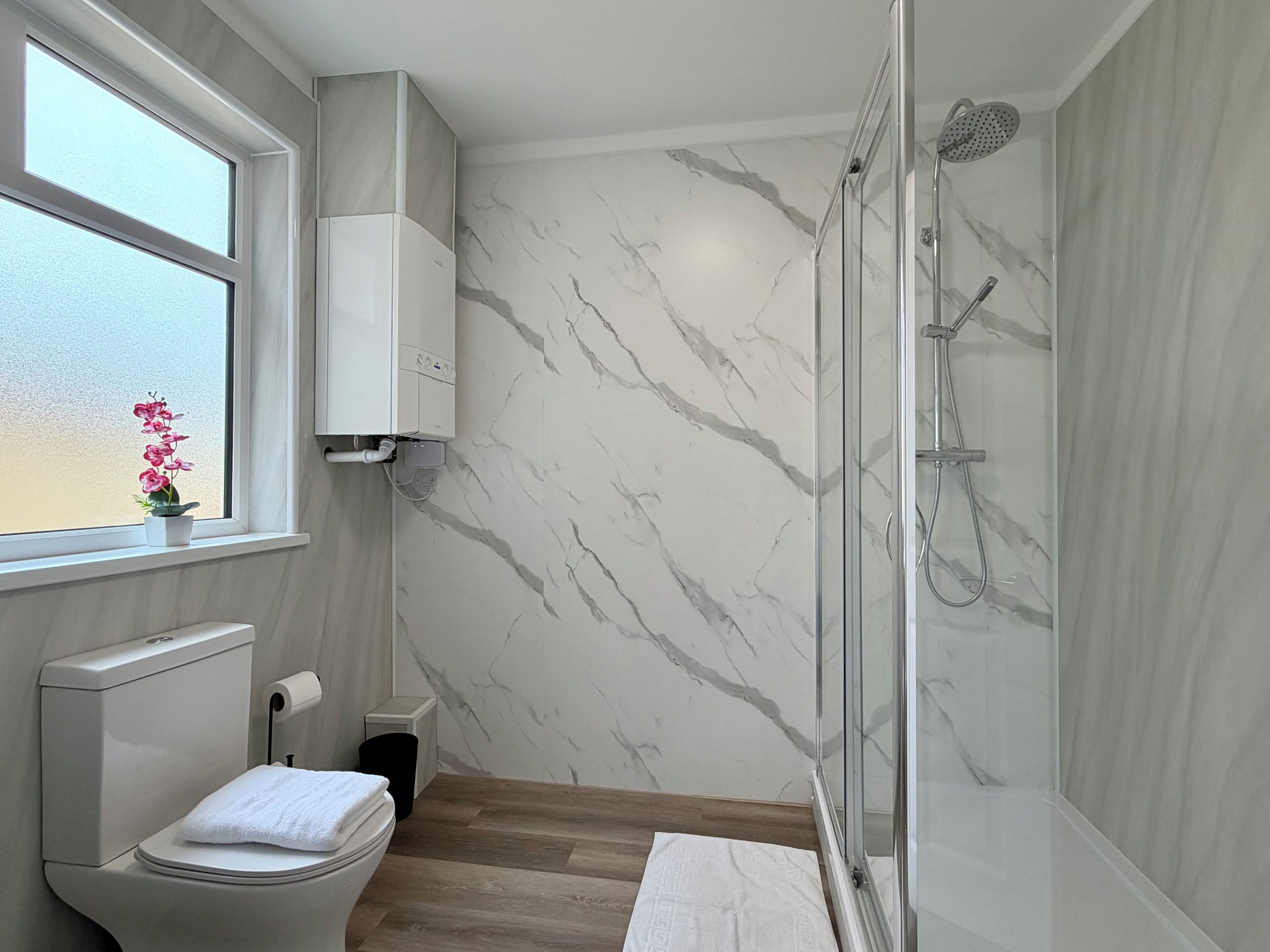 Ein Badezimmer mit Toilette, Dusche, einer Marmorwand und einem Fenster mit Pflanze.