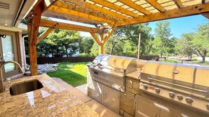 Cocina exterior con encimera de piedra, parrilla integrada y una pérgola.