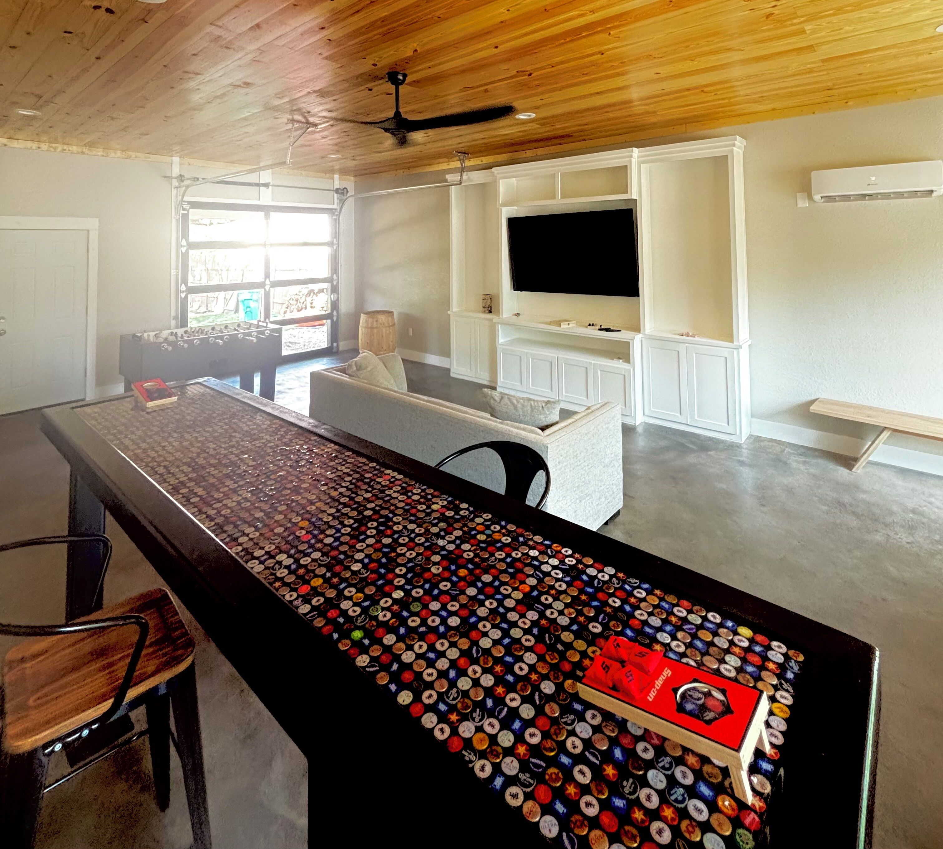 A modern kitchen with a central island covered in bottle caps, a dining area with a sofa, and a TV mounted on the wall.