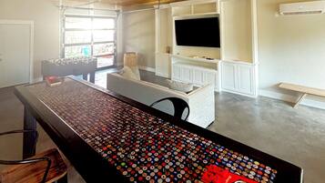 A modern kitchen with a central island covered in bottle caps, a dining area with a sofa, and a TV mounted on the wall.