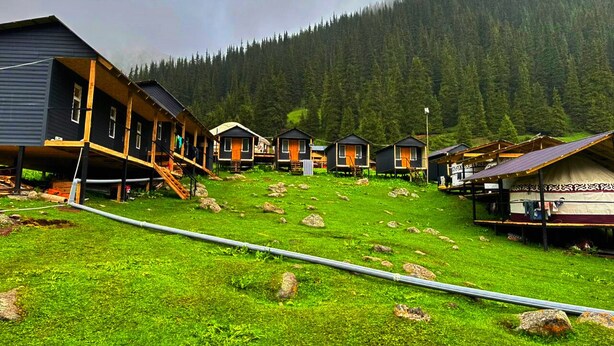 Une rangée de cabanes dotées de terrasses en bois, avec un champ verdoyant au premier plan.