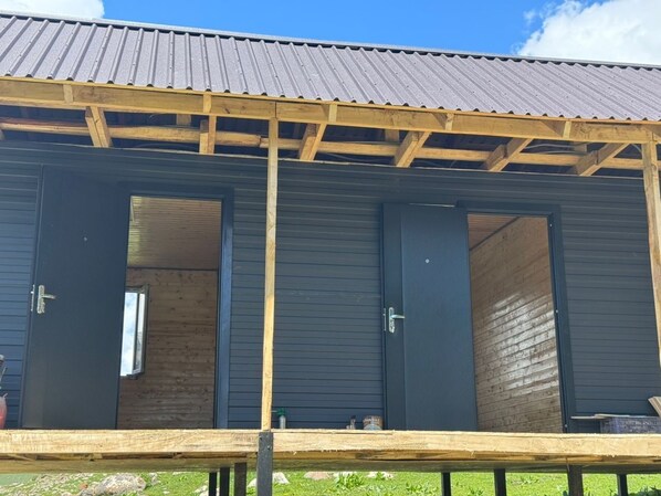 A building with three open doors, a wooden deck, and a metal roof.
