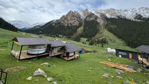 Un chalet de montagne rustique doté de plusieurs cabanes, d’un bateau et offrant une vue panoramique sur les montagnes.