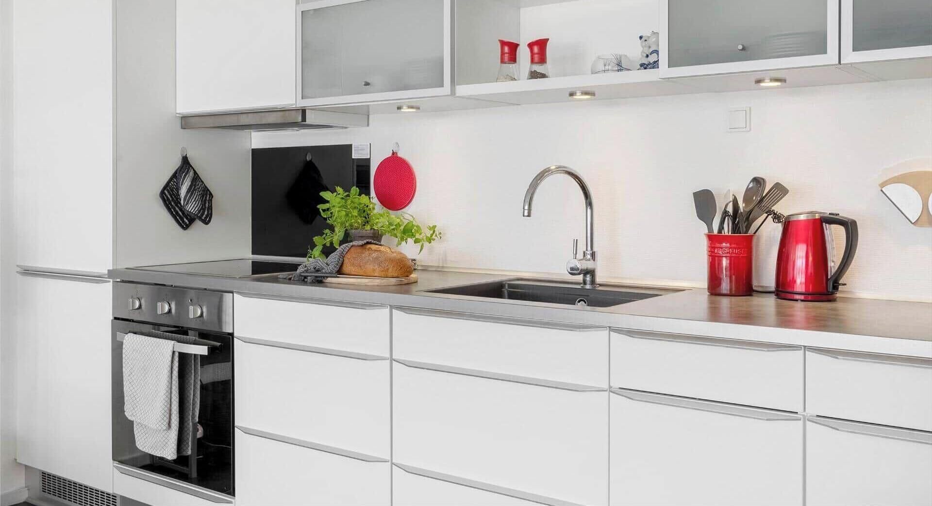 A modern kitchen with a stainless steel sink, a built-in oven, and a countertop with a red kettle and utensils.