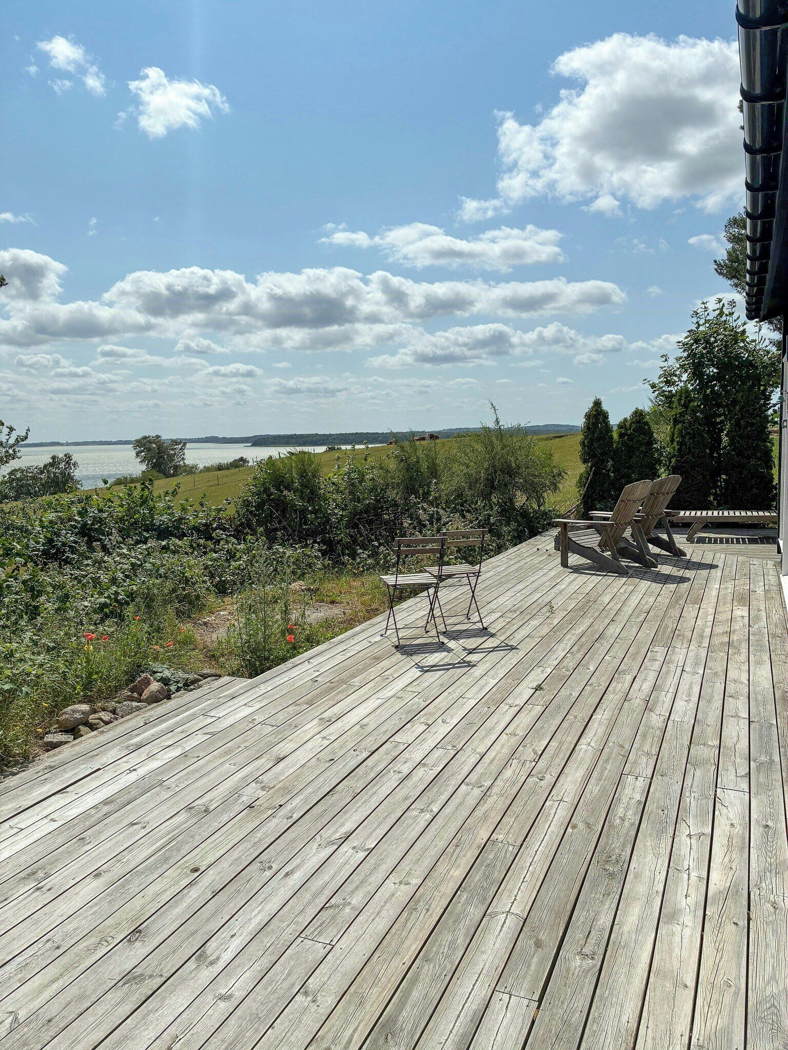 Terraza de madera con sillas y una mesa, con vistas al agua y vegetación.