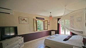 Une chambre à coucher avec un lit, un téléviseur posé sur une commode, une fenêtre donnant sur un beau paysage et un ventilateur de plafond.