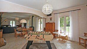 Un salon spacieux avec une table de baby-foot, un canapé, une table à manger, des chaises et de grandes fenêtres.