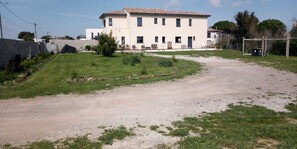 A two-story building with a tiled roof, a paved driveway, and a grassy area with a small tree. - Apartment (Marseillan)