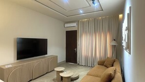 A modern living room with a flat-screen TV, a sofa, a coffee table, and a wall-mounted air conditioner. - Chulis Apartment  (Galadimawa)