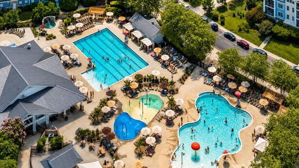 An aerial view of a resort with multiple swimming pools, lounge areas, and a large building complex. - Bayside 3BR Condo | Pool, Golf & Beach Access (Selbyville)