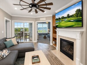 A living room with a fireplace, a television mounted on the wall, and a view of a golf course through the window.