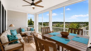 A covered patio with a ceiling fan, a wooden table with chairs, a sofa with cushions, and a view of a residential area. - Bayside 3BR Condo | Pool, Golf & Beach Access (Selbyville)