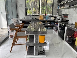 A modern kitchen with a marble countertop, wooden chairs, and a view through large windows. - A Luxurious 5-Bedroom Kids friendly Private Villa in the Heart of Watamu. (Kilifi)