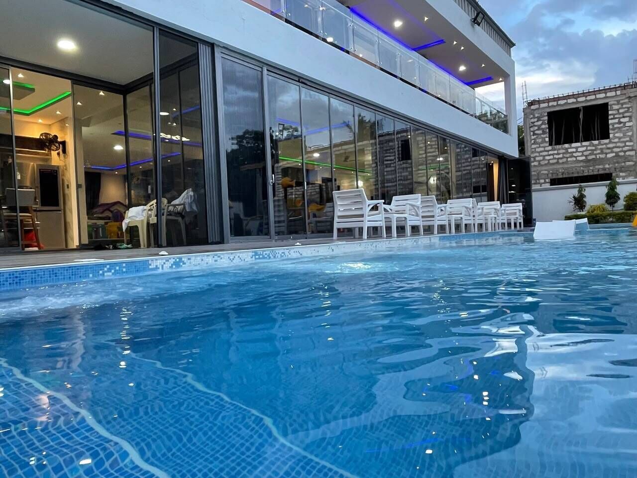 Un hotel moderno con piscina, puertas de cristal y un edificio de piedra al fondo.