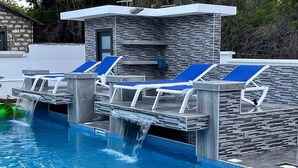 A swimming pool with blue lounge chairs and a stone wall. - A Luxurious 5-Bedroom Kids friendly Private Villa in the Heart of Watamu. (Kilifi)