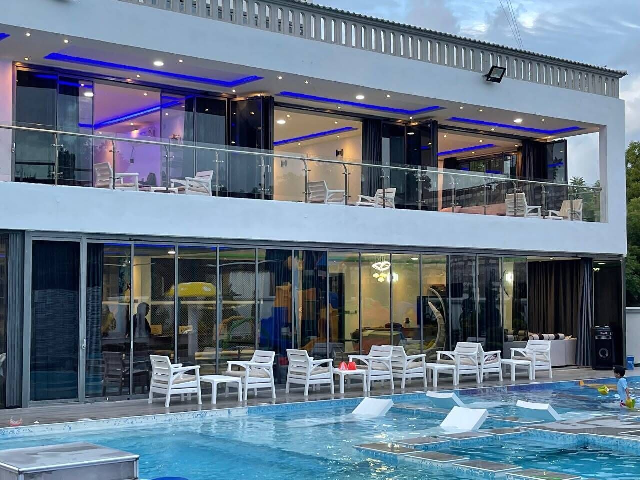 A modern two-story building with a swimming pool, lounge chairs, and glass doors.