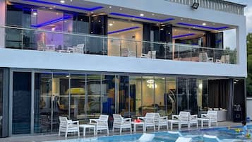 A modern two-story building with a swimming pool, lounge chairs, and glass doors.